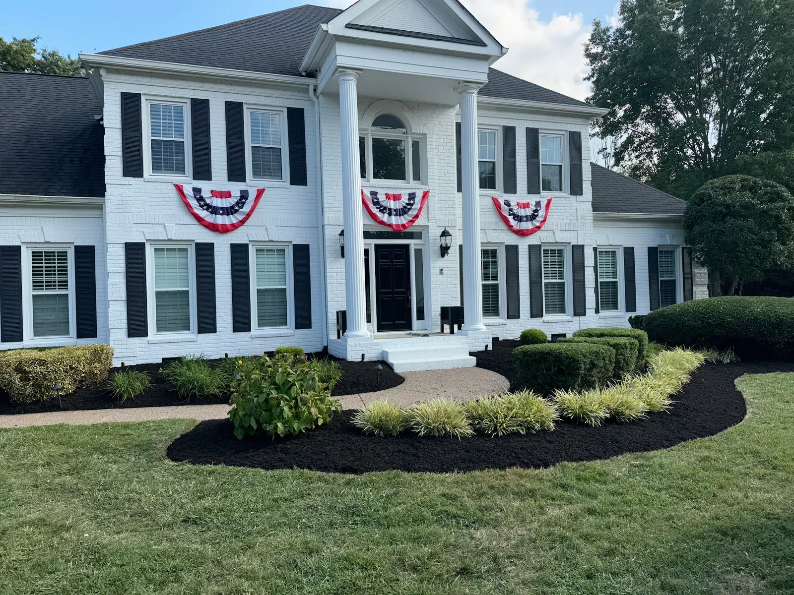 Mulch bed with shrubs in front of a white columned house
