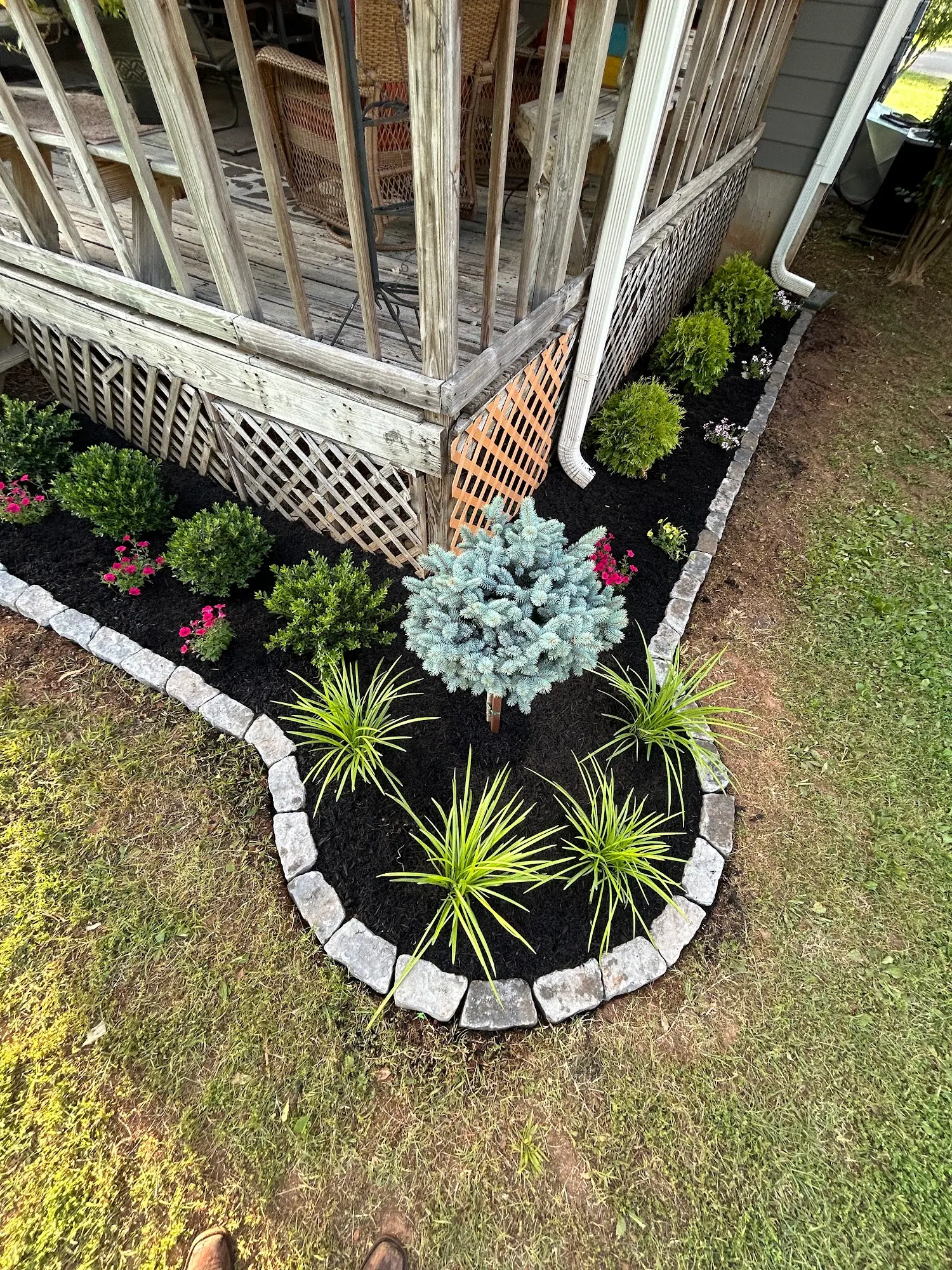 Stone-edged mulch bed with spiky plants at a porch corner